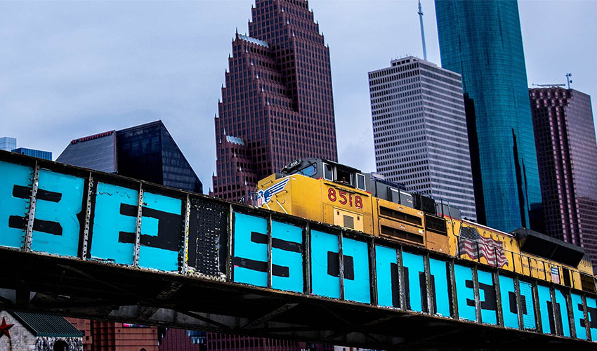 Picture of Houston buildings and train tracks with the painting "Be Someone".