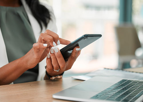 Person sitting at a computer typing something into their cellphone