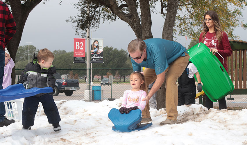 Grandparent  pushing his granddaughter down the snow hill