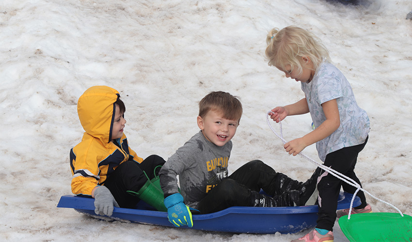 Three kids sliding down the snow hill