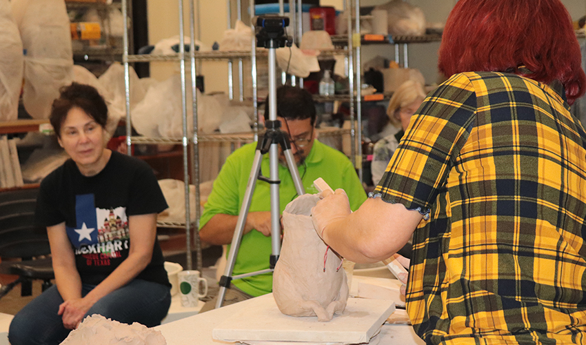 Students observing Mrs. Jeanne making a sculpture.