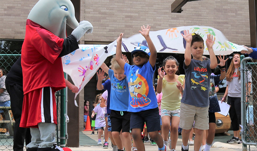 Children run through the Lab School playground reopening banner.