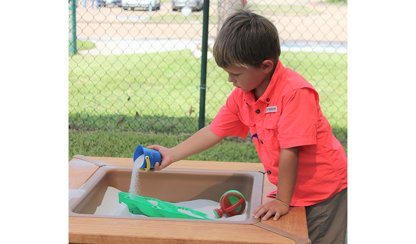 One little boy plays in wooden outdoor sand table.