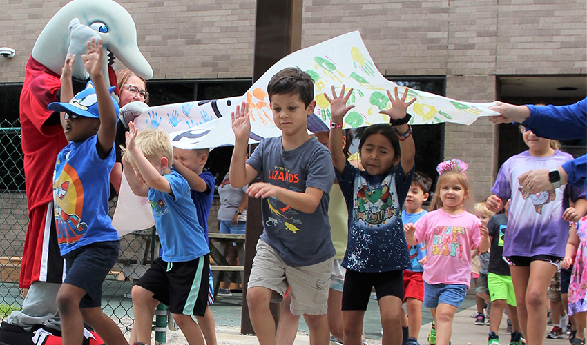 Children run through the Lab School playground reopening banner.