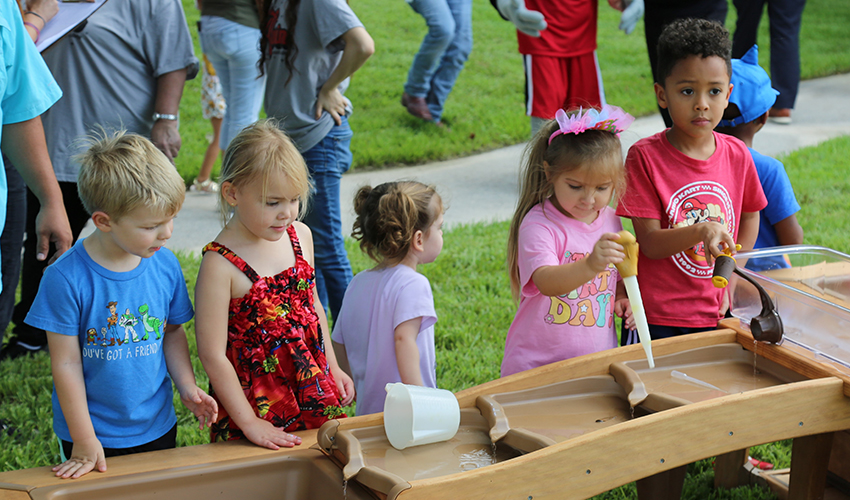Five children play with a wooden outdoor cascade water table.