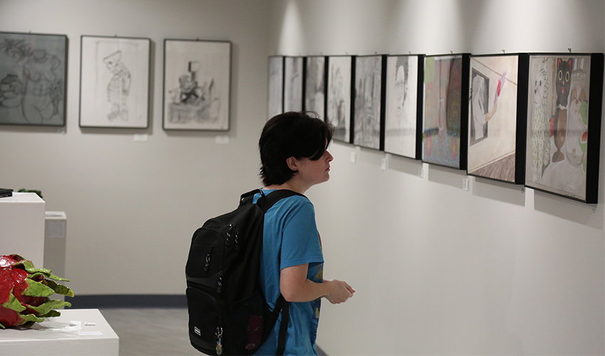 Student admiring the art frames hanging on the wall.