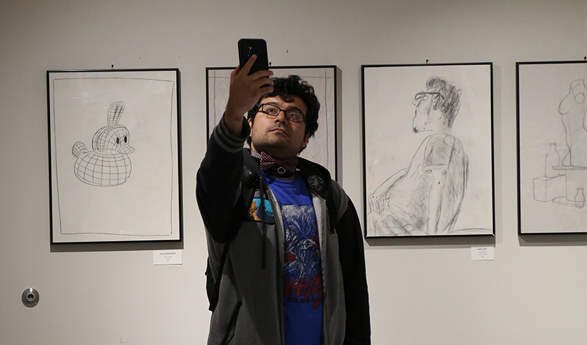 Student taking a selfie with the black and white art drawings.