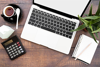 Desk with a open laptop, notebook, calculator, coffee and spiky agave plant.